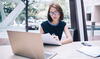 a woman sitting at a table with a laptop reading a document